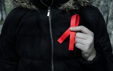 girl in a black jacket holds a red ribbon, as a symbol for the fight against AIDS.