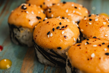 A close up of fresh maki covered with orange sauce, garnished with black sesame seeds, on a blue plate