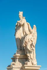 Ancient statue of a monk with angel at the Charles Bridge in Prague at blue sky, Czech Republic, summer, closeup