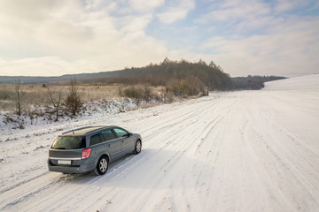 Plakat Family car driving on a dirt road in snow covered winter field.