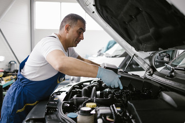 Fototapeta na wymiar Car service mechanic worker standing in front of car engine open hood and working