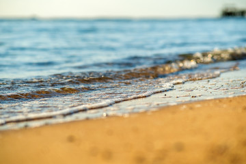 Close up of small sea waves with clear blue water over yellow sand beach at summer sunny shore.