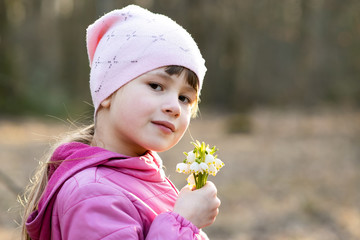 Portrait of happy child girl holding bunch of early spring snowdrops flowers outdoors.
