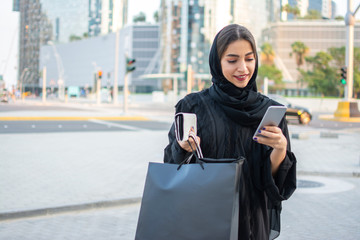 Beautiful muslim woman using phone while walking on street after shopping