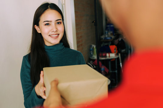 Happy Young Asian Woman Customer Smiling Receive Parcel Post Box From Home Delivery Service Man In Red Uniform At Home, Express Home Delivery Service, Logistics Shipping And Online Shopping Concept