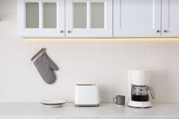 Modern toaster, coffeemaker and dishware on counter in kitchen