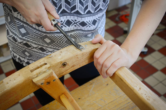 Woman hands in upholstery workshop. Removing old tacks. Working with upholstery tools. Nail remover. Tack lifter removing old nails from wooden construction.