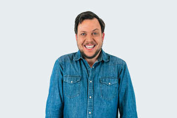 Portrait of young man smiling and looking at camera with one eyebrow raised. Denim shirt and...