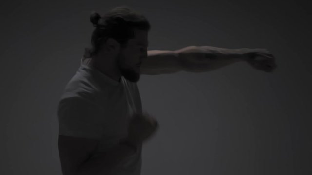 Fighting with darknes. Long haired Fit man in white t-shirt practicing or training, warming up working on camera isolated on white in half light. Slow motion.