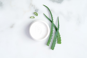 Organic cosmetic skincare moisturizer cream jar and sliced stems aloe vera on marble background. Flat lay, top view. Skin care and beauty treatment concept.