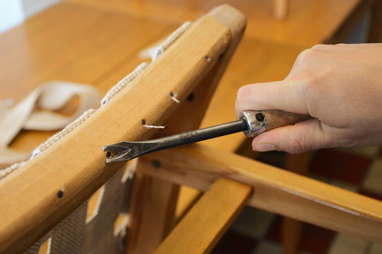 Woman hands in upholstery workshop. Removing old tacks. Working with upholstery tools. Nail remover. Tack lifter removing old nails from wooden construction.