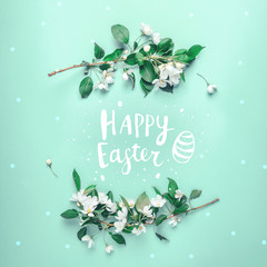 Minimal Easter and spring concept. Lettering Happy Easter in a frame from the flowers of an apple tree on a pastel green background. Flat lay. Concept - Easter minimalism