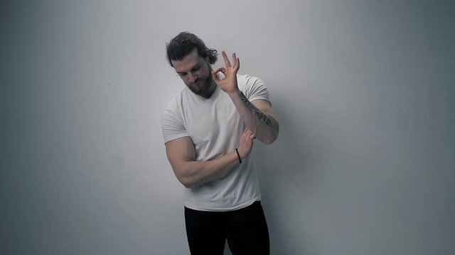 Portrait of a young male looking directly on camera. Bearded caucasian guy wears white t-shirt. Half gray. Darkened light. Slow motion