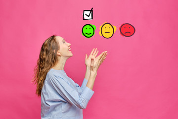 Stylish caucasian girl in a pale blue t-shirt on a pink background. The concept of the highest rating in the form of an emoticon and a check mark.