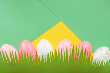 Concept of spring and Happy Easter pink and white with gold eggs on a colorful yellow bright background, grass cut out of paper