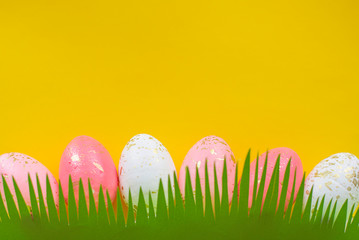 Concept of spring and Happy Easter pink and white with gold eggs on a colorful yellow bright background, grass cut out of paper