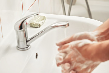 Young man washing hands under tap water with soap, focus on soapbar in background - importance of using lather for proper hygiene concept