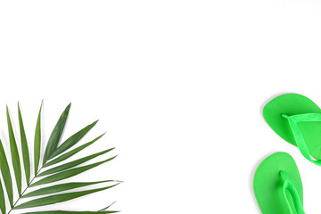 Green palm leaves with flip flop slippers as summer symbols, beachwear on white paper textured background with a lot of copy space for text. Top view, flat lay.