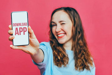 Stylish caucasian girl in a pale blue t-shirt on a pink background. A hand holds a smartphone with...