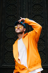 Street needs hip hop dancer in bright orange clothes posing against a dark wall background. Stylish...