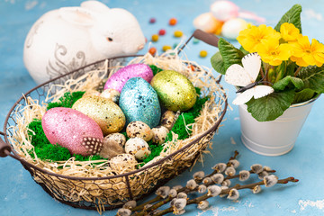 Spring Easter background for holiday. Easter composition with colorful Easter eggs on moss in basket, bunny and spring flower pot. Top view