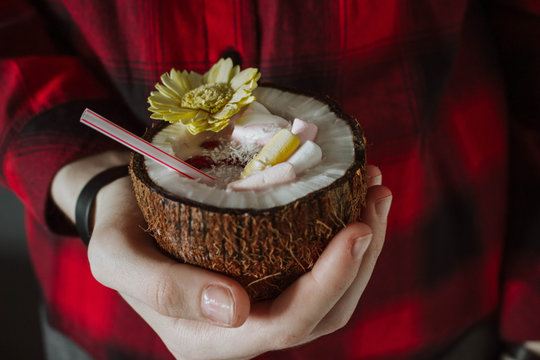 Female hand holding a coconut cocktail with berries and flower