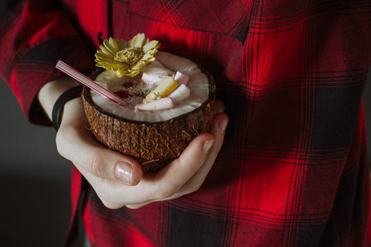 Female hand holding a coconut cocktail with berries and flower