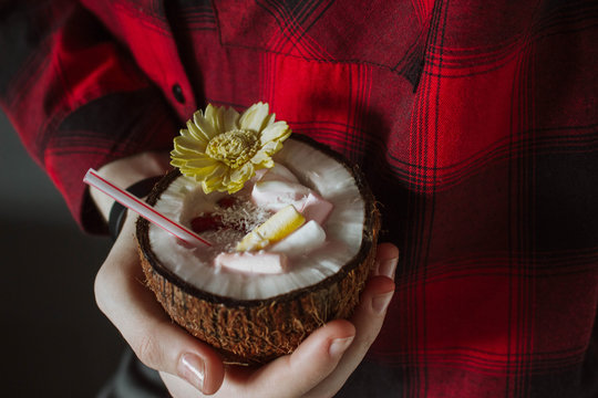 Female hand holding a coconut cocktail with berries and flower
