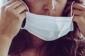 Detail of unrecognizable woman face wearing a white medical face mask. Partly blurred on the edges, light grain. Redhead girl with freckles. Coronavirus, COVID-19 quarantine. Doctor, nurse concept