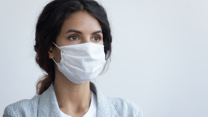 Young attractive serious woman in protective facial medical mask posing over blue background with...