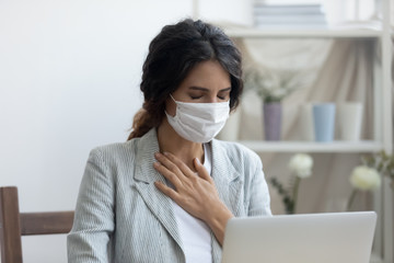 Business woman in mask sitting at desk feels unhealthy put hand where is lungs, suffering from...
