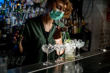 bartender girl pour green liquid from beaker into glass with ice.