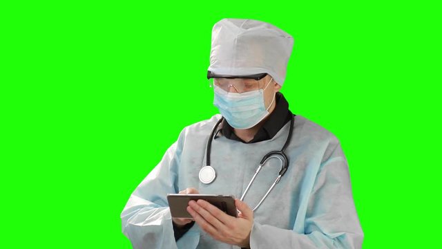 Young doctor in medical mask and protective medical clothing working in mobile phone. Shot on the background of Chrome Key. Chrome Kay high quality