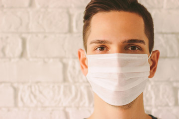 Young professional doctor in protective medical face mask against white wall. Confident medic surgeon wearing white face mask for protection against coronavirus. Preventive measures for COVID-19.