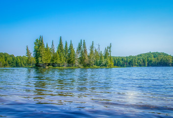 Treed island in blue lake sun reflection nobody © Andre Savary