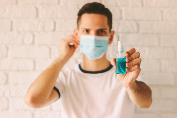 Portrait of young doctor presenting and showing sanitizer bottle in hand as protection against coronavirus COVID-19. Confident man holding antibacterial gel in hand. nCov-19 virus preventive measures