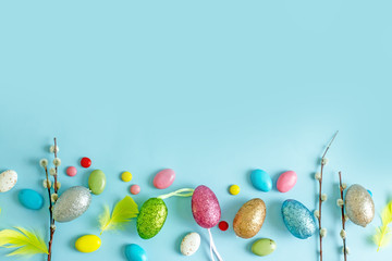 Happy Easter frame with easter eggs,  pussy-willow twigs, colored sweet balls with place for text in the middle on a blue background. Easter background top view,copy space