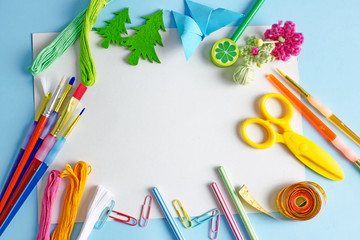 Hobby background. Colorful background about creativity with brushes for drawing, paints, pencils, scissors, origami, paper clips, thread floss on a blue background. Flat lay, save the space, top view