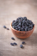 Black raisins in wooden bowl on wood textured background. Copy space. Superfood, vegan, vegetarian food concept. Macro of fresh sweet raisin, selective focus. Healthy snack