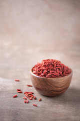 Goji berries in wooden bowl on wood textured background. Copy space. Superfood, vegan, vegetarian food concept. Macro of goji berries, selective focus. Healthy snack.