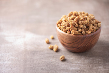 White dried mulberry in wooden bowl on wood textured background. Copy space. Superfood, vegan, vegetarian food concept. Macro of mulberry berries, selective focus. Healthy snack.