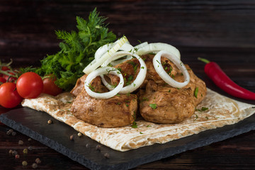 Shish kebabs with vegetables and pita bread on a slate tray in a dark key