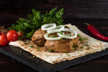 Shish kebabs with vegetables and pita bread on a slate tray in a dark key