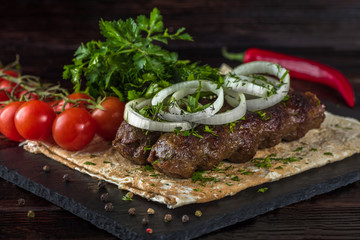 Kebab with vegetables and pita bread on a slate tray in a dark key