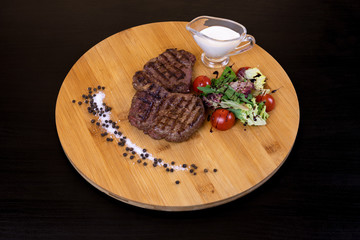 Grilled beef steak with white sauce, cherry tomatoes and rocket salad served on a wooden board