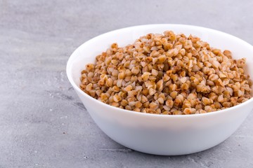 Cooked buckwheat in white ceramic bowl on grey background. Close up, horizontal format.