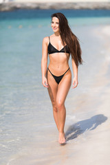 Portrait of happy smiling woman in black bikini walking on the beach.