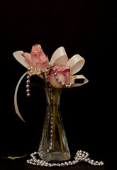 A arrangement of pink roses with ribbon and silver pearls on black background