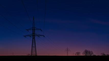 Silhouettes of high voltage pylons at dusk with a clean sky