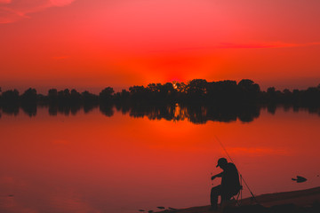 Naklejka na ściany i meble Fisherman at dawn fishing on a fishing rod